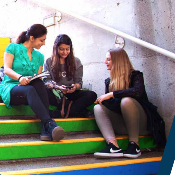 students seated on a stairwell painted with rainbow colours